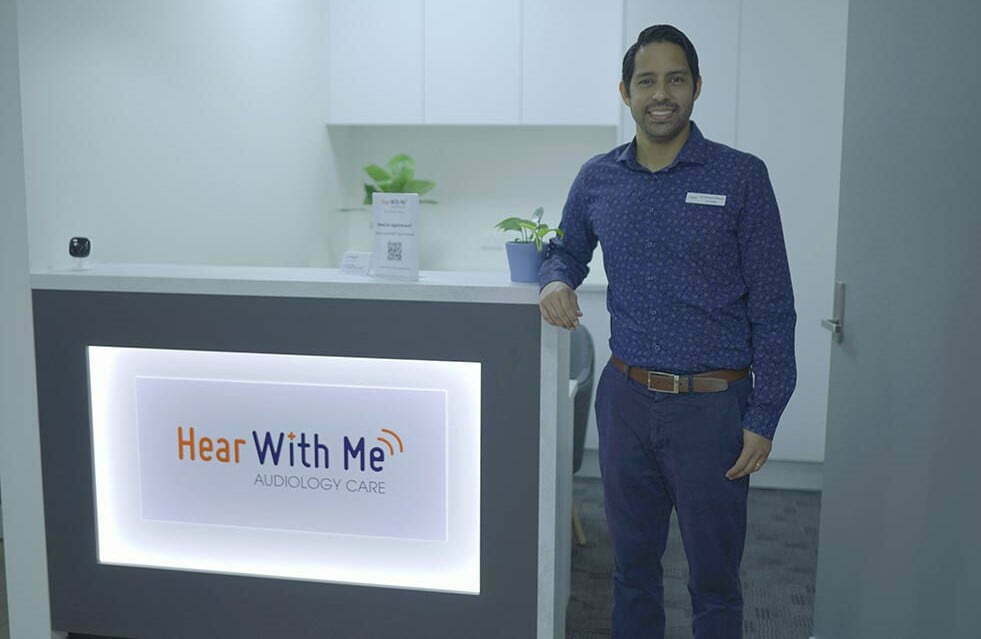 Dr Gerard William standing next to the Hear With Me reception sign